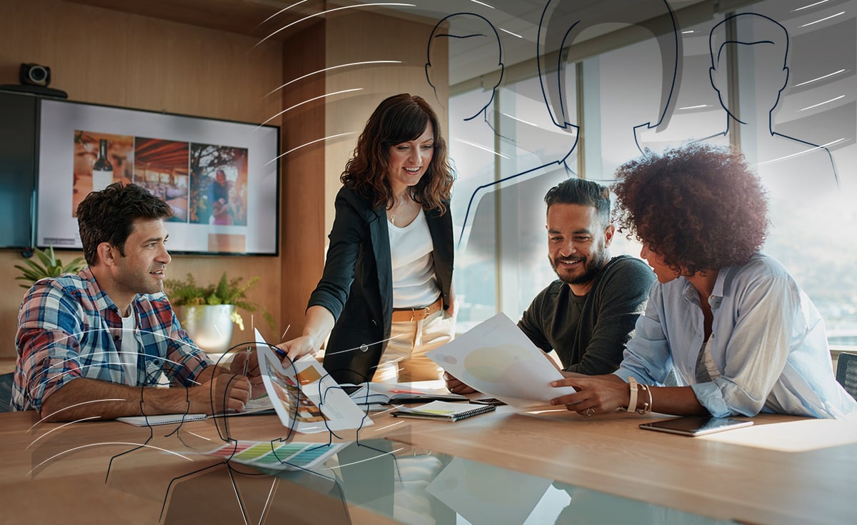 Four coworkers working cooperatively in a conference room. They are gathering around a table. 